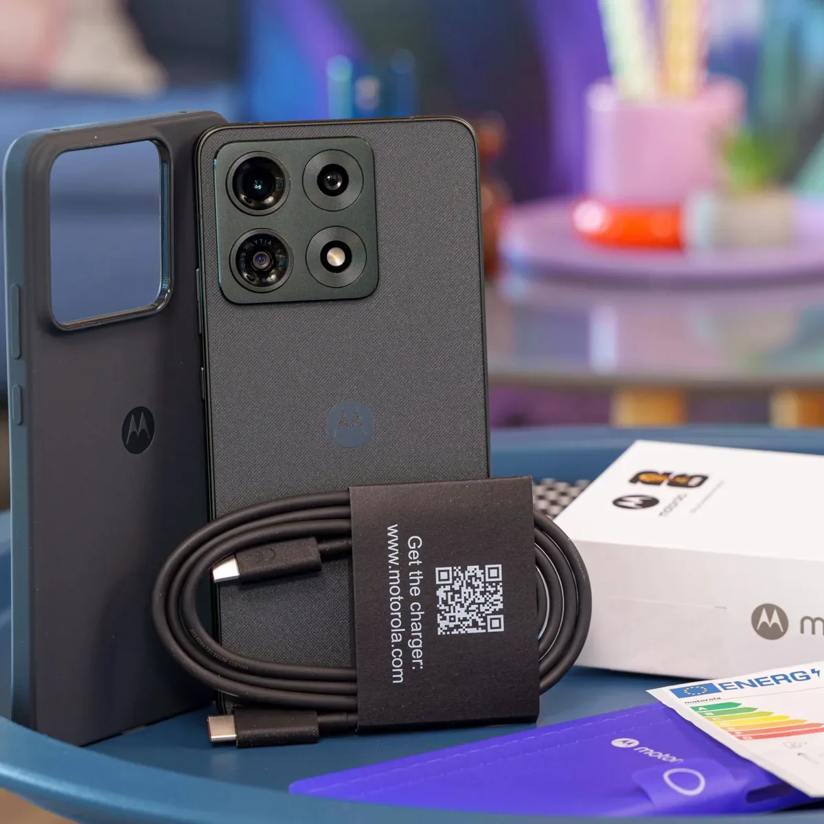 PhonesGate studio photo showing the Moto G86 with box, cable and protective case